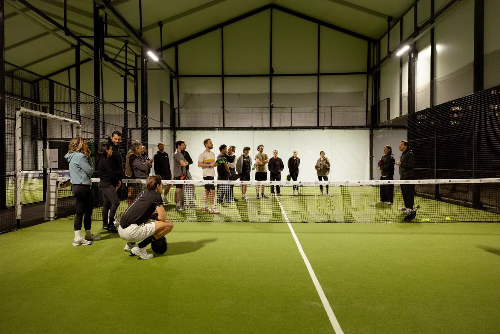 Groupe de joueurs réunis autour du filet lors d'un événement d'entreprise sur le terrain indoor de Padel 15